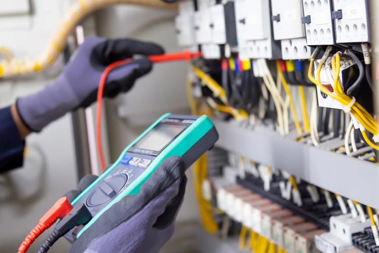 Elektriker med handskar använder digitalt mätinstrument för att testa elkablar och automation