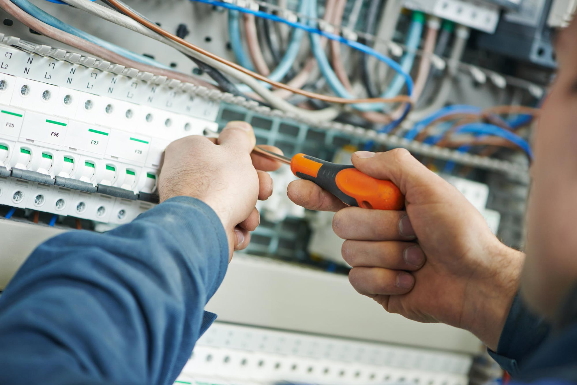 Händer av elektriker med orange-svart skruvmejsel justerar elektrisk utrustning i säkringsskåp